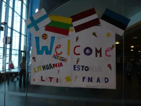 Plakatas „Welcome“ su Lietuvos, Latvijos, Estijos ir Suomijos vėliavomis